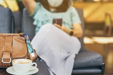 Corona Virüsü 'nü (Covid-19) öldürmek için mini alkol jeli şişesi kafede üzerinde sıcak kahve olan kahverengi deri bir omuz çantasına asılır. Yeni normal yaşam tarzı. Sağlık hizmetleri kavramı. Alkol jeline odaklanın.