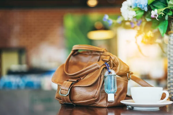 Corona Virüsü 'nü (Covid-19) öldürmek için mini alkol jeli şişesi kafede üzerinde sıcak kahve olan kahverengi deri bir omuz çantasına asılır. Yeni normal yaşam tarzı. Sağlık hizmetleri kavramı. Alkol jeline odaklanın.