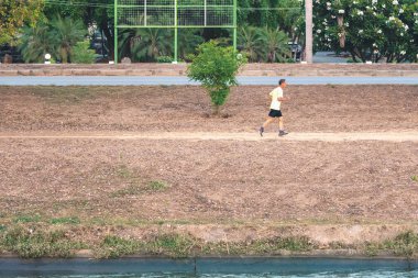KANCHANABURI / THAILAND-MAY 7. 2020: Tayland 'ın Kanchanaburi kentinde 7 Mayıs 2020 tarihinde Mae Klong Barajı' ndaki sulama kanalının yanında sağlıklı bir yolda koşan tanımlanamayan Taylandlı sporcular.
