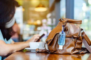 Corona Virüsü 'nü (Covid-19) öldürmek için mini alkol jeli şişesi kafede üzerinde sıcak kahve olan kahverengi deri bir omuz çantasına asılır. Yeni normal yaşam tarzı. Sağlık hizmetleri kavramı. Alkol jeline odaklanın.