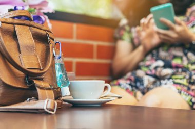 Corona Virüsü 'nü (Covid-19) öldürmek için mini alkol jeli şişesi kafede üzerinde sıcak kahve olan kahverengi deri bir omuz çantasına asılır. Yeni normal yaşam tarzı. Sağlık hizmetleri kavramı. Alkol jeline odaklanın.