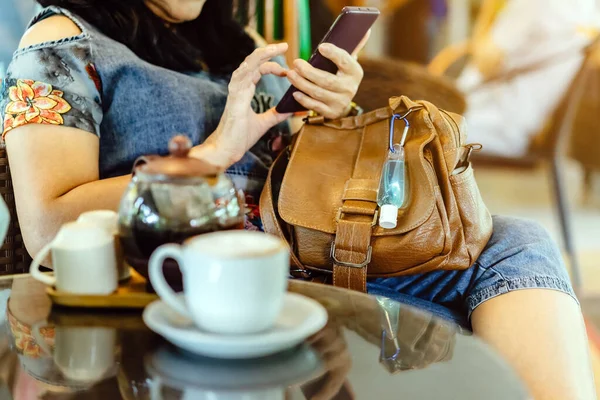 Corona Virüsü 'nü (Covid-19) öldürmek için mini taşınabilir alkol jeli şişesi kafede sıcak kahveli kahverengi deri bir omuz çantasına asılır. Yeni normal yaşam tarzı. Sağlık hizmeti kavramı. Alkol jeline odaklı.