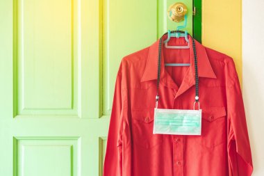 Corona Virüsü 'nün (COVID-19) yatak odasının önündeki kapı kolunda asılı kırmızı gömlekle dolaşmasını önlemek için yeni bir cerrahi maske. İşe gitmeden önce yeni normal yaşam tarzı.