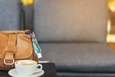 Corona Virüsü 'nü (Covid-19) öldürmek için mini alkol jeli şişesi kafede üzerinde sıcak kahve olan kahverengi deri bir omuz çantasına asılır. Yeni normal yaşam tarzı. Sağlık hizmetleri kavramı. Alkol jeline odaklanın.