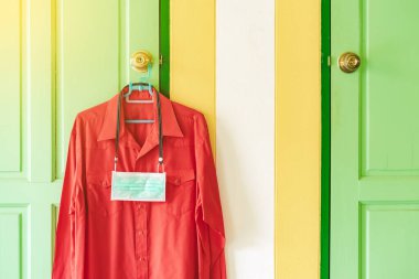 Corona Virüsü 'nün (COVID-19) yatak odasının önündeki kapı kolunda asılı kırmızı gömlekle dolaşmasını önlemek için yeni bir cerrahi maske. İşe gitmeden önce yeni normal yaşam tarzı.