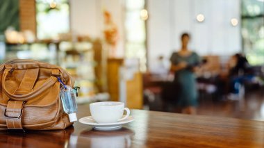 Corona Virüsü 'nü (Covid-19) öldürmek için mini alkol jeli şişesi kafede üzerinde sıcak kahve olan kahverengi deri bir omuz çantasına asılır. Yeni normal yaşam tarzı. Sağlık hizmetleri kavramı. Alkol jeline odaklanın.
