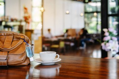 Corona Virüsü 'nü (Covid-19) öldürmek için mini alkol jeli şişesi kafede üzerinde sıcak kahve olan kahverengi deri bir omuz çantasına asılır. Yeni normal yaşam tarzı. Sağlık hizmetleri kavramı. Alkol jeline odaklanın.