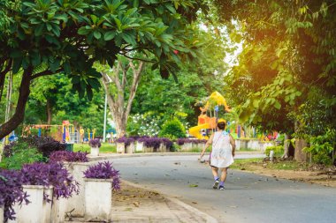 Asyalı yaşlı bir kadının arkası, yürüyüş ve halk parkında sağlık için koşuya giderken kulaklık takar. Doğada kıdemli koşucu. Huzurlu doğanın tadını çıkaran yaşlı bir kadın. Sağlık konsepti.