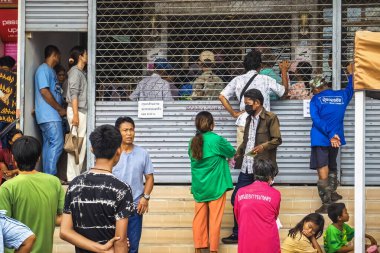 KANCHANABURI, THAILAND-EPTEMBER 27, 2024: Hükümet tasarruf bankası kapanmadan önce para çekmek ve işlemleri tamamlamak için bankanın önünde kuyrukta bekleyen Taylandlı tanımlanamayan kalabalık.