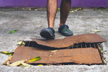Yaya ayakları sandalet giyer hasarlı kanalizasyon borularının üzerinde yürür ve paslı çelik plakalarla kaplıdır. Rögar kapağı kırılmış. Yoldaki çukur. Paslı rögar kapağı. Şehirdeki kanalizasyon kapağındaki kaza..