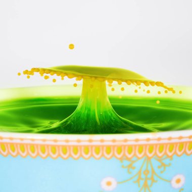 Sarı ve yeşil damla dekoratif bir kaba çarpıştı bir şemsiye şeklinde su. Sarı renkli süt yeşil sıvı içine düştü.