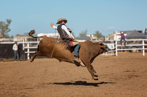 A cowboy competing in a bull riding event at a country rodeo