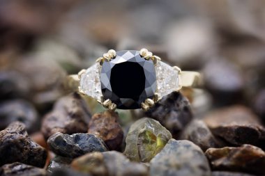 Büyük bir siyah elmas elmas üstünde ikisinden biri yan kesme ve kesilmemiş değerli taşlar yığını üzerinde yalan parlak beyaz trilyon ile sarı altın ringe ayarla