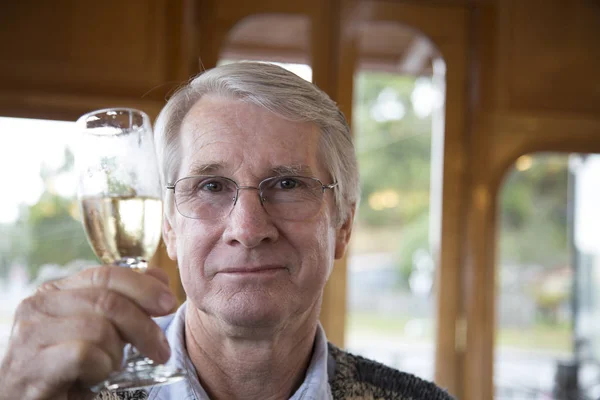 A senior male retiree lifts his glass of wine for a toast with a smile as he boards a train for a holiday