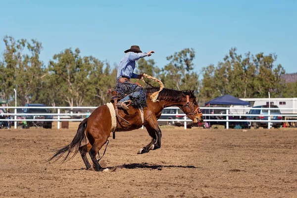 Cowboy riding a bucking bronco horse in a competition at a country rodeo