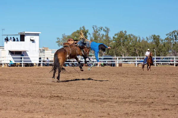 Cowboy riding a bucking bronco horse in a competition at a country rodeo