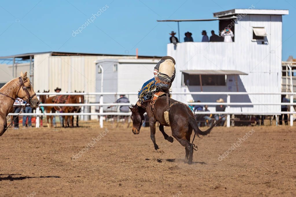 Cowboy riding a bucking bronco horse in a competition at a country rodeo