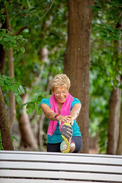 Senior woman with towel around neck exercising stretching warming up outdoors in a forest