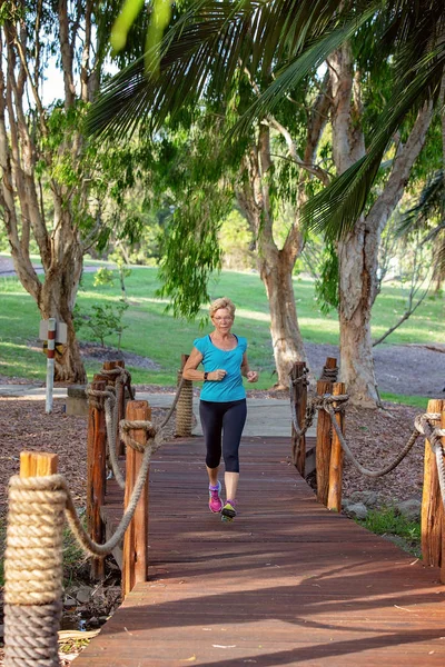 Senior woman in fitness clothing exercising running jogging outdoors on a wooden bridge in a park