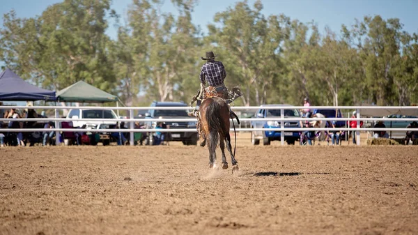 Cowboy rides a wildly bucking horse in bareback bronc event at a country rodeo