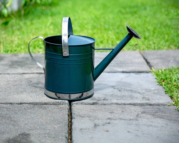 Green metal watering can on grey stone paving blocks in a garden