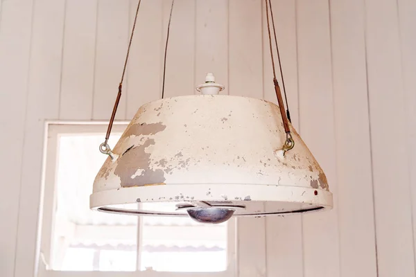 A vintage worn hanging ceiling light with peeling paint against a cream wall