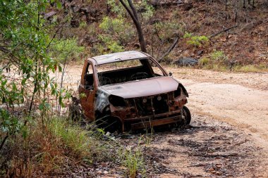 Yanmış bir araba enkazı, toprak bir dağ yolunda terk edilmiş.