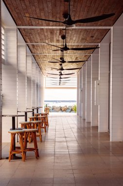 Sahil manzarasına açılan masa ve sandalyelerle dolu koridor.