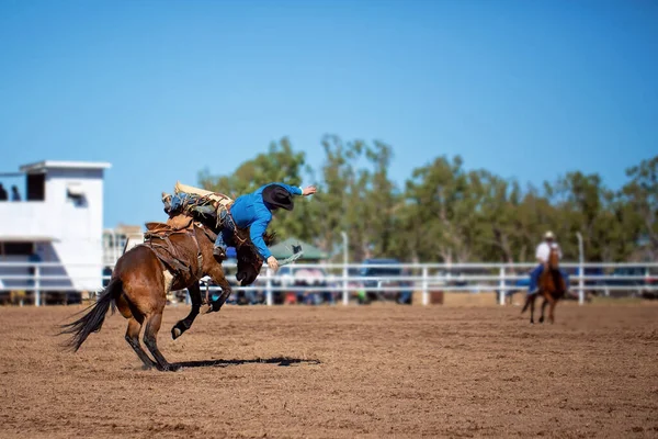 A cowboy riding a bucking bronco horse at an Australian country rodeo