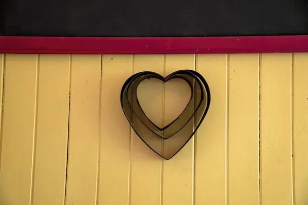 Three heart shaped cake tins hanging on a vintage timber wall as a decorative display item