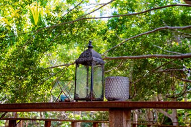 Bahçe ortamında yayılan dallara karşı ahşap bir çitin üzerinde antika fener ve mum tutacakları.