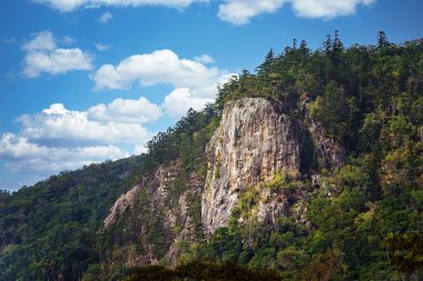 Volkanik çekirdek dağı, bulutlu mavi bir arka planda bitki örtüsüyle kaplı.