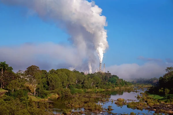 Smoke from the chimney of a sugarcane mill on a creek bank