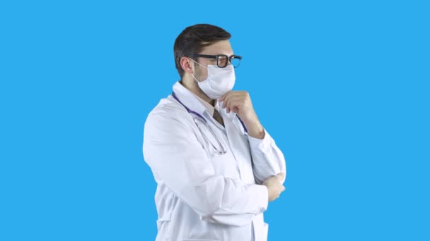Portrét doktora v lékařském plášti a masce si myslí, že drží ruku na bradě. — Stock video