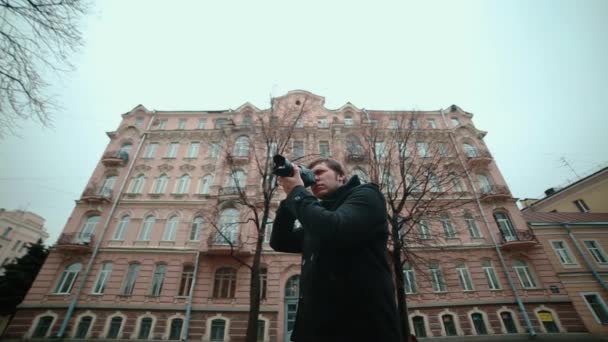 Фотограф в черном пальто делает снимки с камеры во время съёмок в разных направлениях . — стоковое видео