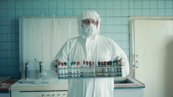 Porträt eines medizinischen Mitarbeiters in Anzug und medizinischer Maske hält eine Schachtel mit Reagenzgläsern in den Händen. — Stockvideo