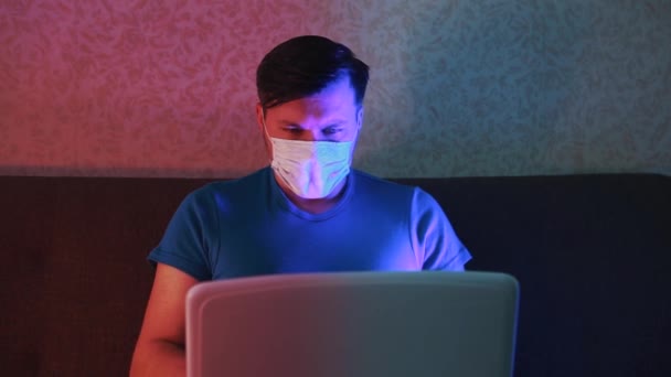 Um homem mascarado em quarentena trabalha remotamente num computador. . — Vídeo de Stock