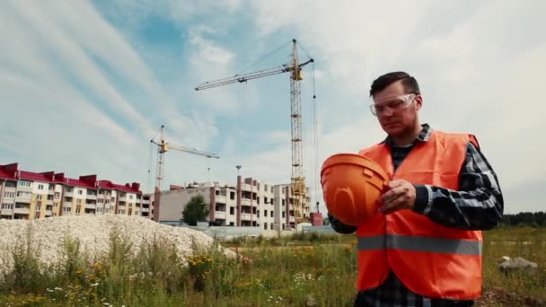 Retrato de un constructor masculino en una obra de construcción se pone un casco . — Vídeos de Stock