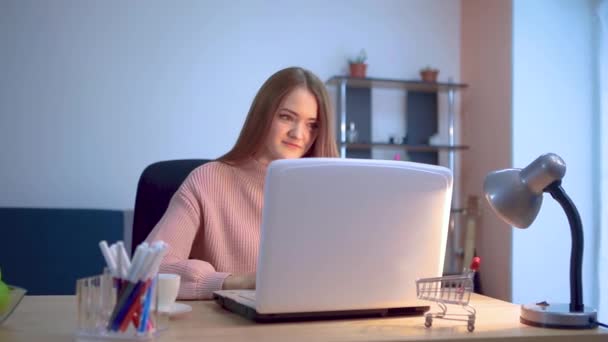 Chica joven que trabaja en una computadora portátil sentada en una mesa en un trabajo remoto, ingresa datos sonriendo desde una tarjeta de crédito . — Vídeos de Stock