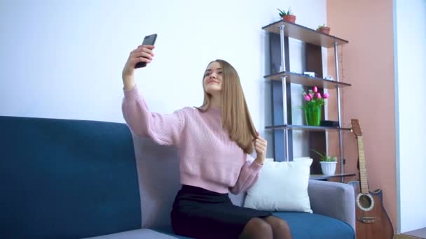 Mädchen sitzt auf der Couch macht Selfie glättet ihr Haar. — Stockvideo