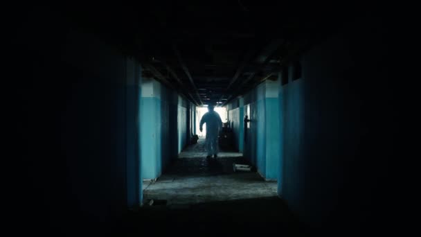 Een man in een beschermend pak en bril loopt door een verlaten donkere gang en kijkt om zich heen.. — Stockvideo