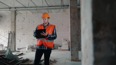 Erkek bir inşaat işçisi bir odada duruyor ve tablet klasörüne veri yazıyor..