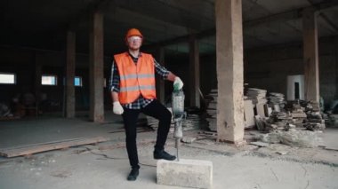 Turuncu yelek giymiş bir inşaatçının portresi ve arka planda bir inşaat alanında elinde çekiç tutan turuncu bir miğfer..