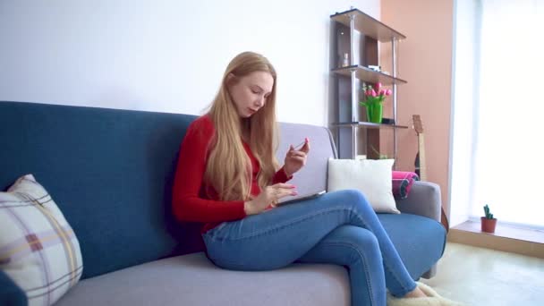 En ung flicka som sitter i en soffa matar in data från ett kreditkort i telefonen. — Stockvideo