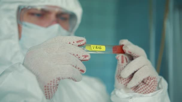 En läkare i skyddsglasögon håller ett provrör med COVID-19-viruset i sina händer. — Stockvideo