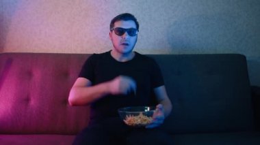 Kanepede oturan bir adam üç boyutlu bardakta cips yiyor..