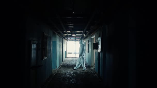 Un hombre con traje protector y gafas en un pasillo oscuro en un viejo laboratorio pasa de una puerta a otra . — Vídeos de Stock