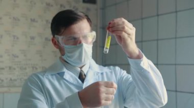 Koruyucu gözlüklü bir doktor elinde COVID-19 virüsünün salladığı bir test tüpü tutuyor..