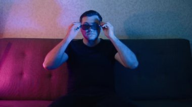 Adam yavaşça 3D gözlüklerini takıyor ve televizyon izliyor..