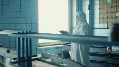 Laboratuar teknisyeni koruyucu giysi ve gözlüklerle laboratuvar penceresinde duruyor ve verileri kaydediyor..